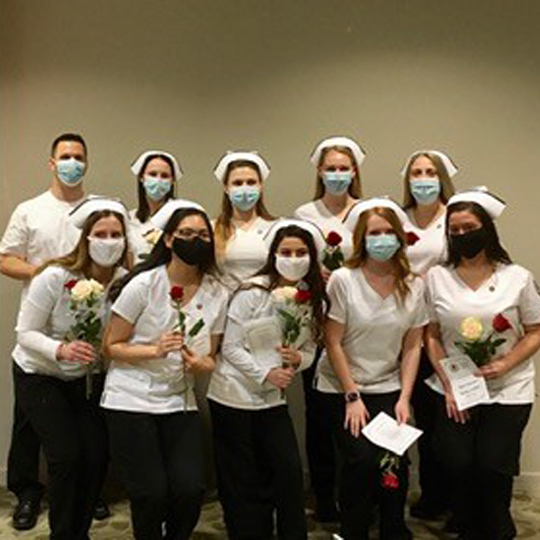 Nurse graduates gather in a group all wearing masks after their ceremony.
