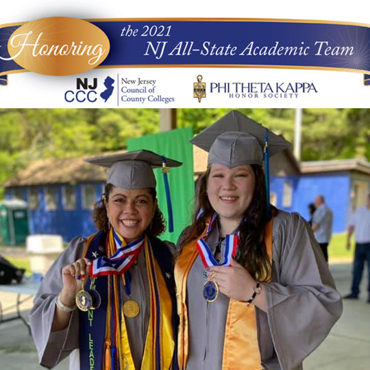 Two female graduates stand holding up their Phi Theta Kappa metals.