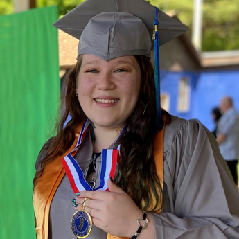 female graduate proudly shows off her Phi Theta Kappa medallion.