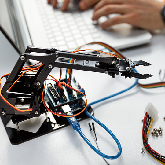image of a small robotics project on a desk with a person typing on a laptop.