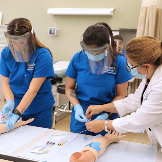 Female medical assistants are instructed to take blood by the professor.