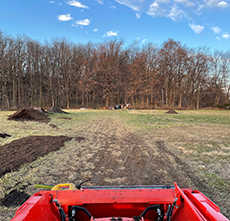 A view of the student farm with dirt piles from the back of a red truck.