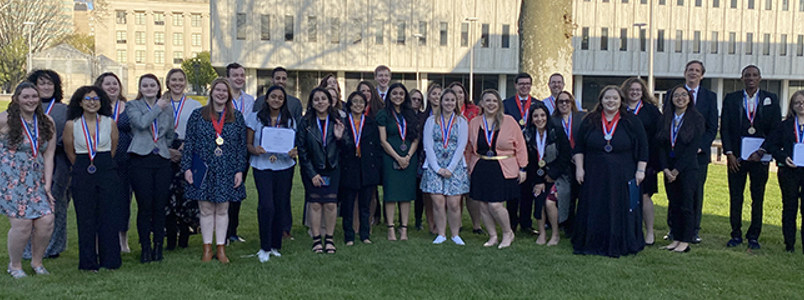 Students and staff stand outside a building holding their awards