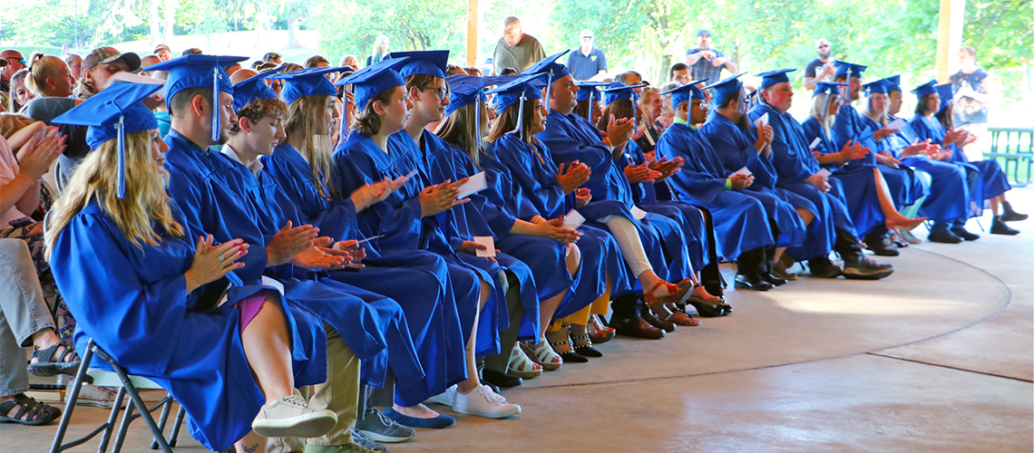 Students sit in blue caps and gowns at graduation