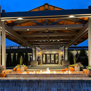 The exterior of a restaurant at night with a fire pit and fall decor.
