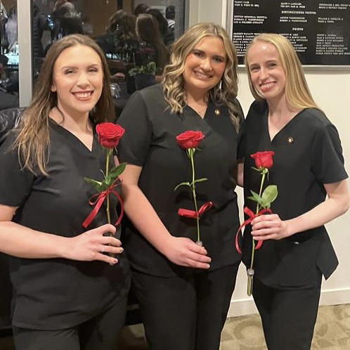 Three Nurse graduates gather holding roses