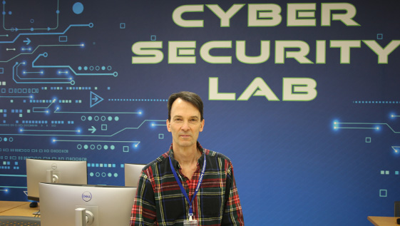 Man sits on a desk in the cyber security lab.