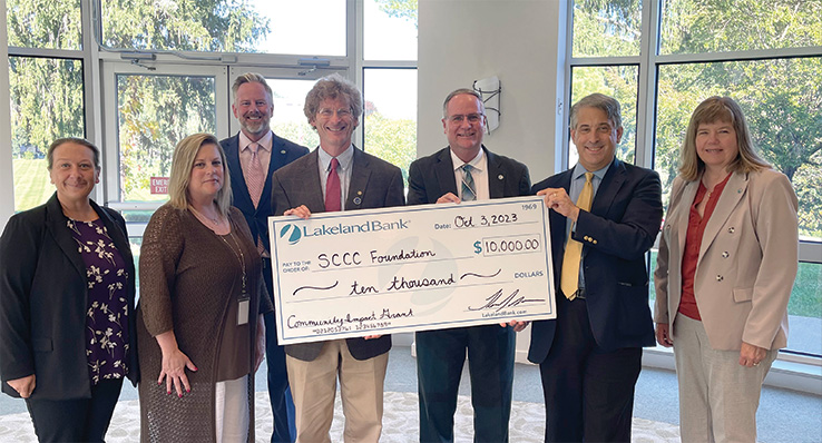 Professional men and women pose with a large donation check.