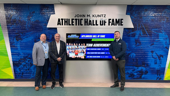 three men standing in front of a Hall of Fame Wall.